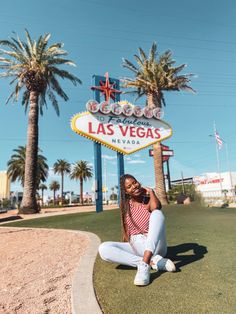 a woman sitting on the ground in front of a las vegas sign and palm trees