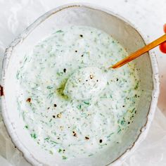 a person holding a wooden spoon in a white bowl filled with green liquid and herbs