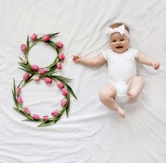 a baby is laying next to a wreath made out of pink tulips on a white sheet