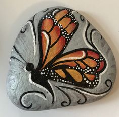 a painted rock with an orange and black butterfly sitting on it's back side