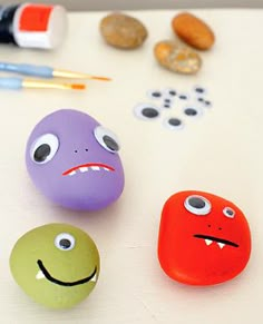 three rocks with faces painted on them sitting next to paintbrushes and other items