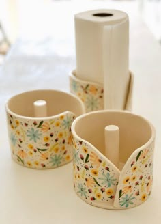 three flowered cups are sitting on a table next to a roll of toilet paper