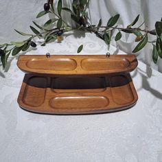 a wooden tray with two compartments on the bottom and an olive branch in the background