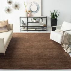 a living room with two white chairs and a brown area rug on the floor in front of a couch