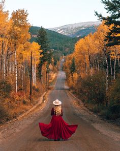 a woman in a red dress and hat is walking down the road with her back to the camera