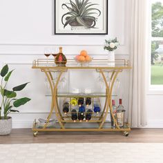 a gold bar cart with wine glasses and bottles on it in front of a window