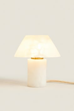 a white table lamp with a light on top of it and a cord attached to the base