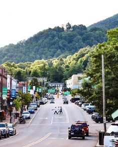 a city street with cars and people walking on the side walk, trees in the background