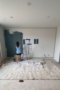 a woman is painting the walls in an empty room with white carpet and blue paint