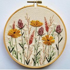 an embroidery project with yellow and red flowers on it's hoop hanging from a wall