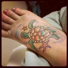 a person with a tattoo on their arm holding a small turtle and starfish in the background