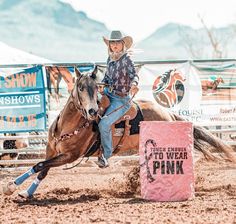 a woman riding on the back of a brown horse next to a pink sign in an arena