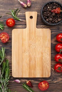 a cutting board surrounded by tomatoes and herbs