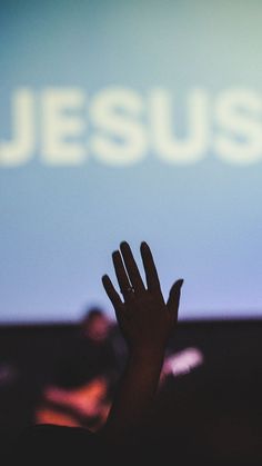 someone holding their hand up in front of a screen with the word jesus on it