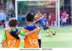 two young boys in orange and blue soccer uniforms standing on the field with their arms around each other