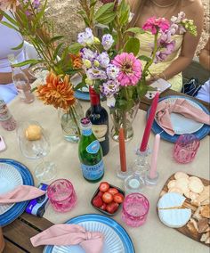 the table is set with pink and blue plates, silverware, flowers, wine bottles, and napkins