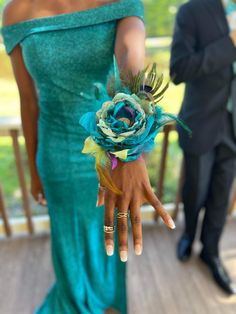 a woman in a blue dress holding a flower on her hand with another man in the background