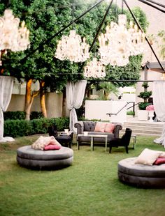 an outdoor living area with couches, tables and chandeliers hanging from the ceiling