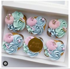 cupcakes decorated with pastel blue and pink icing in a white box