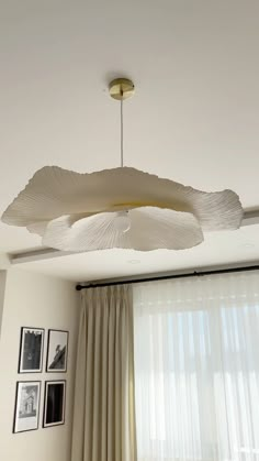 a white ceiling light hanging from the ceiling in a living room with curtains and pictures on the wall