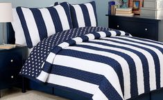 a bed with blue and white striped comforter in a small room next to a night stand