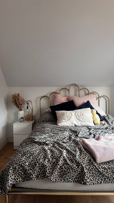 a bed with leopard print sheets, pillows and blankets on it in a white room