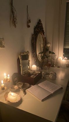 an open book sitting on top of a table next to candles and other items in front of a mirror