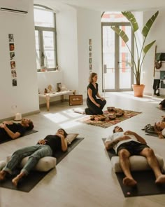 a group of people laying on their stomachs in a room with yoga mats and potted plants