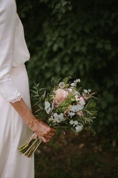 a woman holding a bouquet of flowers in her hand and wearing a white wedding dress