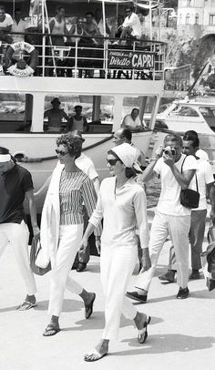 black and white photograph of people walking on the street in front of a boat with passengers