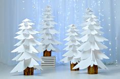 three white paper christmas trees in front of a curtain