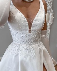 a woman wearing a white dress with pearls on it