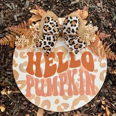 a hello pumpkin door hanger on the ground with leaves and flowers around it that says hello pumpkin