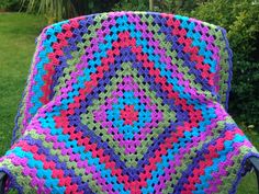 a colorful crocheted blanket sitting on top of a lawn chair in the grass