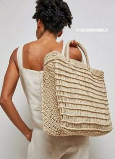 a woman carrying a straw bag with her back turned to the camera while standing against a white wall