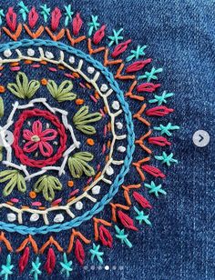 an embroidered piece of cloth with flowers and leaves in the center on a blue jean jacket