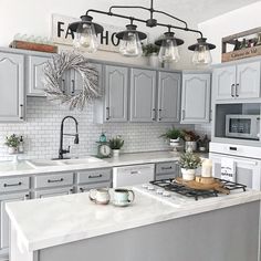 a kitchen with gray cabinets and white counter tops is decorated with hanging lights above the stove