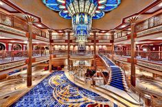 the inside of a cruise ship with stairs and chandeliers on each floor,