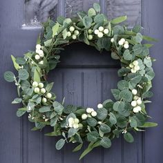 a green wreath with white berries and leaves hanging on a blue front door, ready to be decorated for christmas