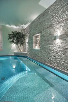 an indoor swimming pool with stone walls and blue tiles on the floor, next to a tree