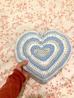 a crocheted heart on a bed with someone's hand holding it up