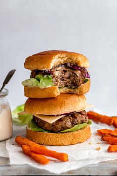 two hamburgers stacked on top of each other next to carrot sticks and a jar of ranch dressing