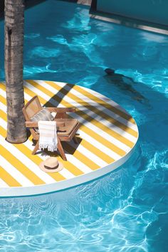 a chair and table in the middle of a swimming pool with palm tree next to it