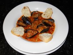 a white plate topped with mussels and bread on top of a black table