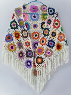 a crocheted shawl with fringes and flowers is hanging on a hook