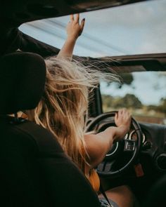 a woman sitting in the driver's seat of a car with her hand on the steering wheel