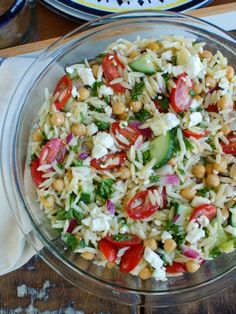 a glass bowl filled with pasta salad on top of a wooden table