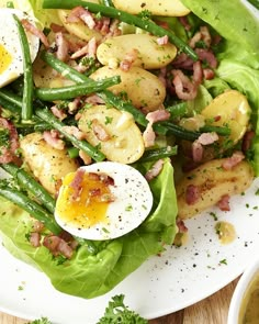 a white plate topped with lettuce and potatoes covered in bacon next to an egg