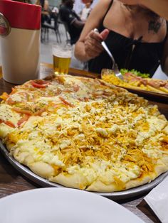 a large pizza sitting on top of a pan covered in cheese and toppings next to a drink