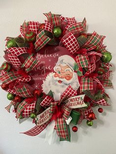 a christmas wreath hanging on the wall with santa claus's face and green ornaments